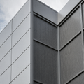 Metallfassade aus grauen Blechpaneelen mit regelmaessiger Fugenteilung, teilweise perforiert