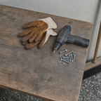 Arbeitshandschuhe, Akkuschrauber und Schrauben auf einer Holzbank – Symbolbild zum Aufbau